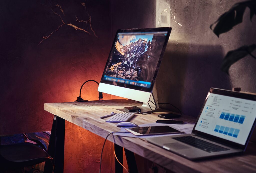 Scenic image of a laptop and computer monitor on a wooden desk in ambient orange lighting