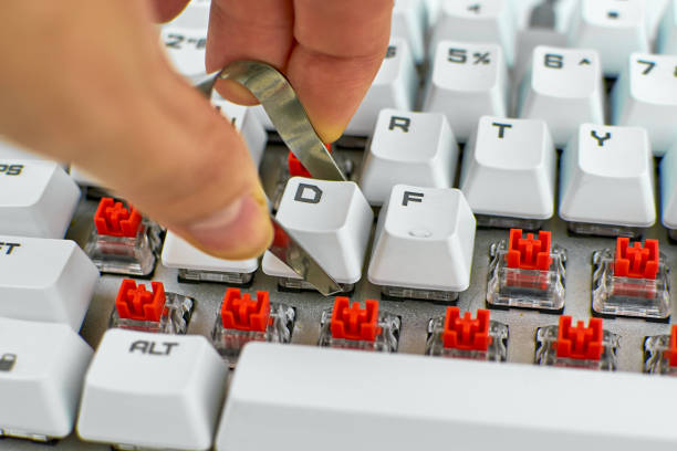Close-up of a man's hands using tweezers to remove a keyboard keycap to clean the device