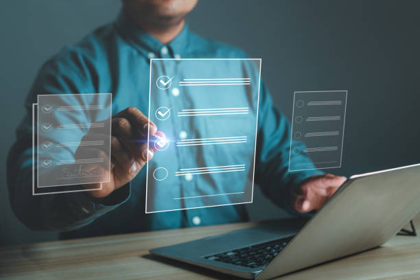 A businessman in a blue shirt in front of an open laptop signing an electronic document on a digital virtual screen using a stylus pen